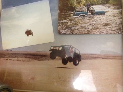 1984 Ford Bronco - Off-road vehicle airborne over a sandy terrain. Another vehicle is visible in a river.