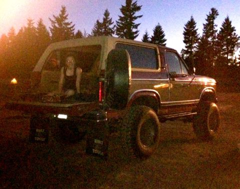 1984 Ford Bronco - A maroon and tan Ford Bronco is parked outdoors at dusk with a person sitting in the open tailgate.