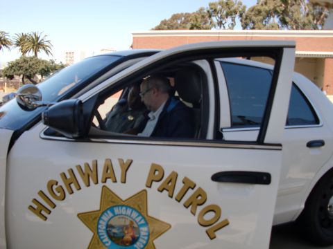 1991 Ford LTD Crown Victoria - Two men are inside a white California Highway Patrol car, with the driver's side door open.