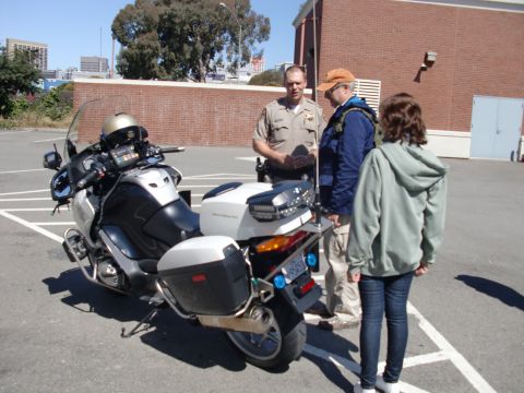 1991 Ford LTD Crown Victoria - A police officer speaks with two civilians next to a parked motorcycle.