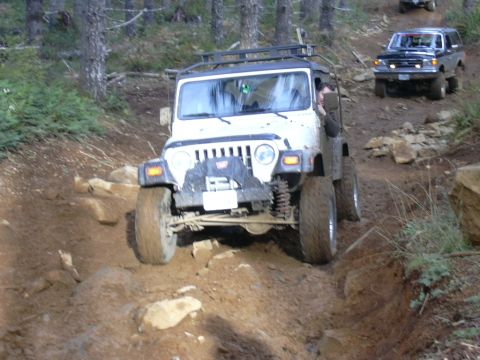 1991 Ford Bronco - Two off-road vehicles navigate a challenging dirt path through a wooded area.