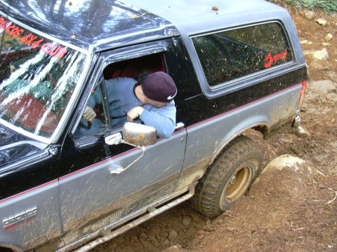 1991 Ford Bronco - A driver maneuvers a muddy Ford Bronco through a challenging off-road terrain.