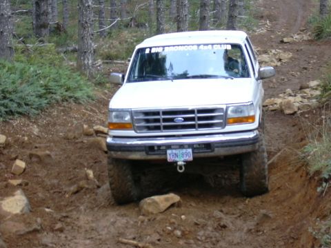 1991 Ford Bronco - A white Ford Bronco navigates a challenging muddy and rocky off-road trail.