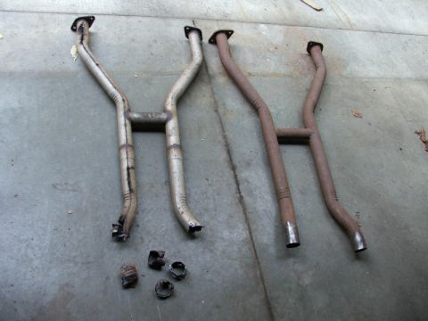 1988 Ford Crown Victoria LTD - Two pairs of exhaust pipes, one set silver and one set rusted brown, lie on a concrete surface.