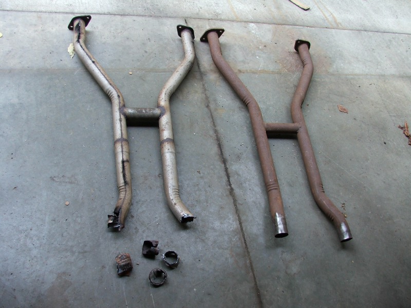 Two pairs of exhaust pipes, one set silver and one set rusted brown, lie on a concrete surface