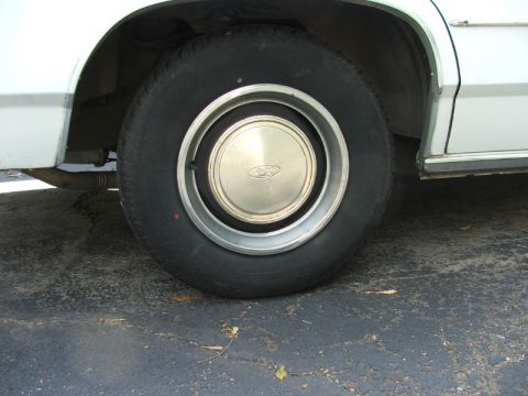 1988 Ford Crown Victoria LTD - A close-up view of the rear wheel and fender of a white vehicle, a Ford-branded hubcap.