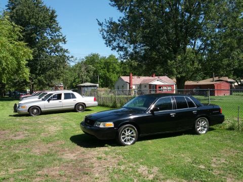 2007 Ford Crown Victoria - Two Ford Crown Victorias are parked in a grassy yard on a sunny day.