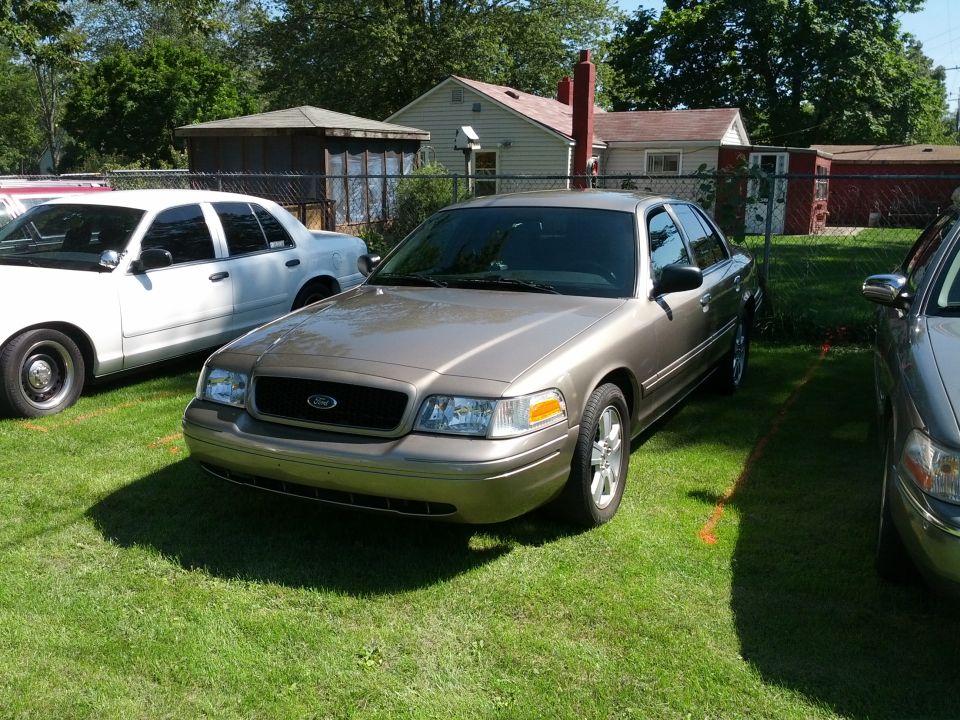 Tan 2007 Ford Crown Victoria front 3/4 view parked on grass next to other vehicles