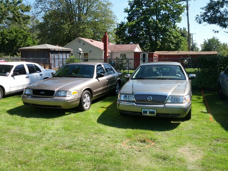 Two sedans parked on a lawn. One is a Ford Crown Victoria, the other appears to be a Mercury Grand Marquis