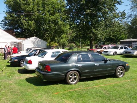 2007 Ford Crown Victoria - Several sedans are parked on a grassy lawn under trees on a sunny day.