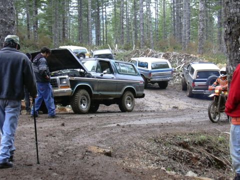 1991 Ford Bronco - Several Ford Broncos and a dirt bike are gathered on a muddy road in a forest.