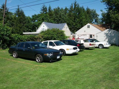2007 Ford Crown Victoria - Several Ford Crown Victoria Police Interceptors are parked on the grass on a sunny day.