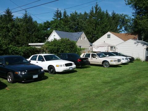 2007 Ford Crown Victoria - Several Ford Crown Victorias are parked in a grassy yard with houses in the background.