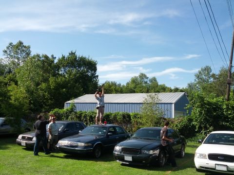 2007 Ford Crown Victoria - A group of people and several cars are gathered on a grassy lawn under a blue sky with clouds.