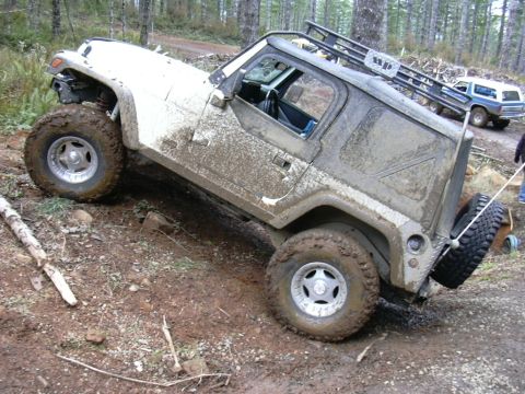1991 Ford Bronco - A white Jeep Wrangler is stuck on a muddy trail, while another vehicle waits behind it.