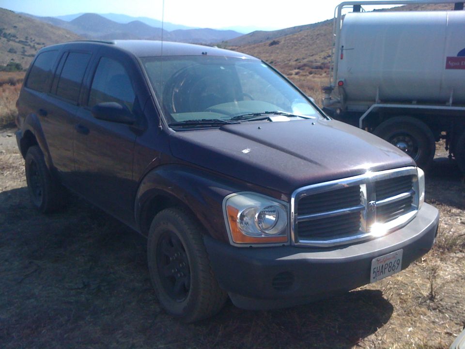 Dark red Dodge Durango SUV parked on dirt, front quarter view. License plate 5HAP869 visible