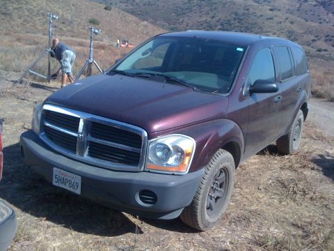 1968 Ford Mustang - A maroon Dodge Durango SUV is parked on a dirt road, with filming equipment and crew visible in the background.