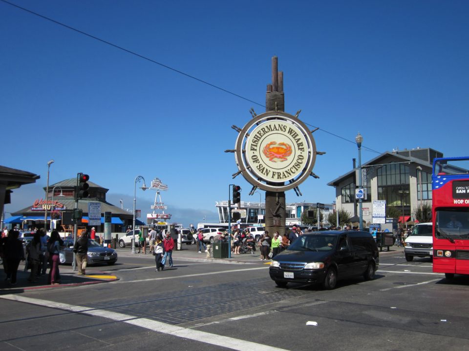 Black minivan driving on a street with a Fisherman's Wharf sign in the background