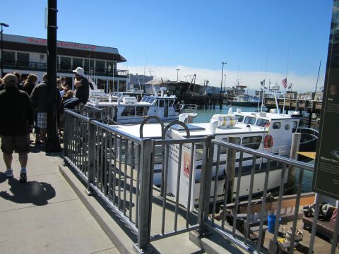 1991 Ford LTD Crown Victoria - A view of several boats docked at a pier on a sunny day, with people visible on the walkway.