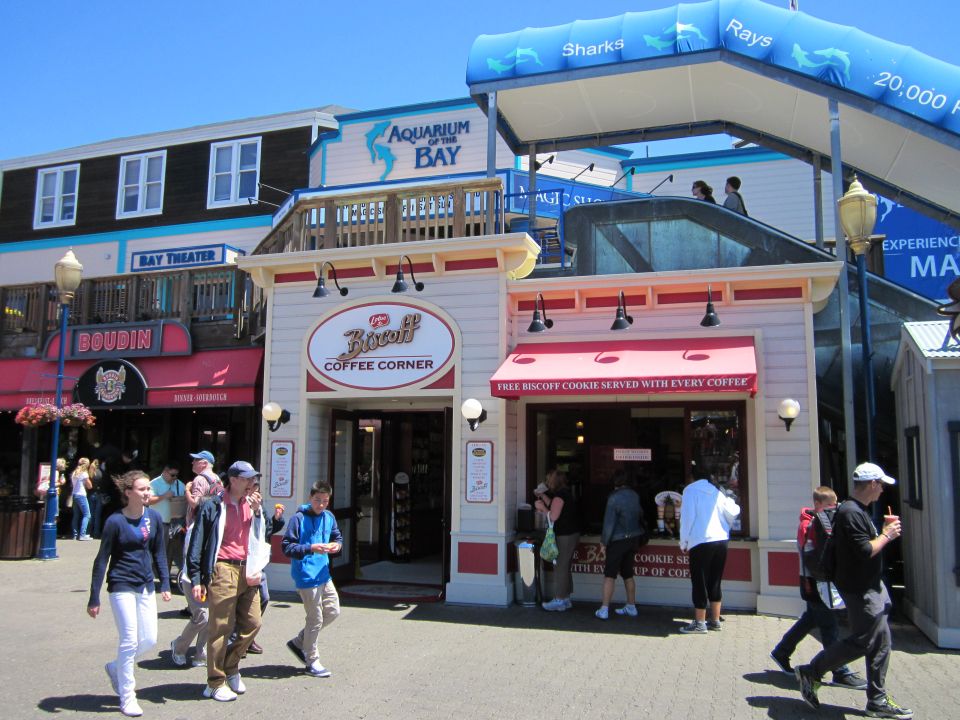 Aquarium of the Bay and Boudin Bakery shops on a sunny day with people walking by