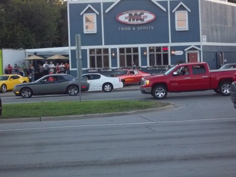 1970 Ford Ranchero - A red pickup truck is seen driving on the road in front of a restaurant.