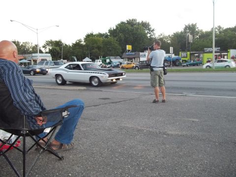 1970 Ford Ranchero - A photographer captures a classic muscle car as it cruises by, observed by a spectator.