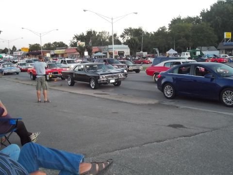 1970 Ford Ranchero - A man photographs a black muscle car in a lot filled with other vehicles, possibly at a car show.