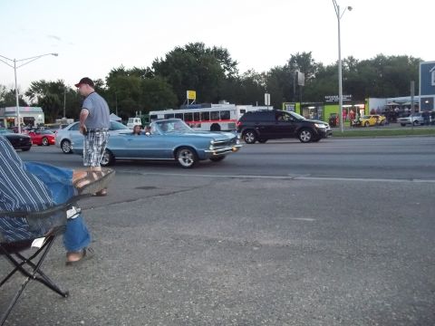 1970 Ford Ranchero - A blue convertible cruises down the street with other vehicles and pedestrians present.