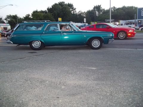 1970 Ford Ranchero - A teal station wagon drives down the road next to a red sports car.