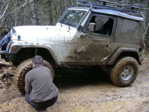 1991 Ford Bronco - A person inspects a heavily mud-covered Jeep Wrangler on a dirt road.
