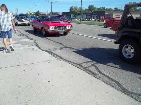 1970 Ford Ranchero - A red 1970 Ford Ranchero is seen driving on a sunny day, with other vehicles and pedestrians present.