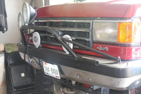1990 Ford Bronco - Front view of a red 1990 Ford Bronco, equipped with a chrome grille, auxiliary lights, and a custom light bar.