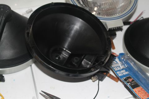 1990 Ford Bronco - A disassembled headlight housing sits on a workbench next to a headlight assembly and a tube of sealant.