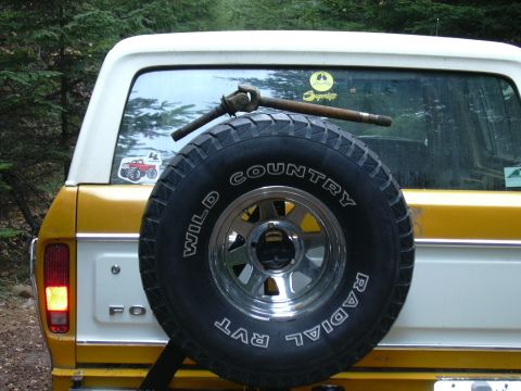 1991 Ford Bronco - Spare tire on the back of a Ford Bronco, with a driveshaft and stickers visible on the window.