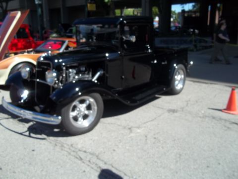 1970 Ford Ranchero - This black 1930s pickup truck is parked outdoors with other vehicles and an orange cone.