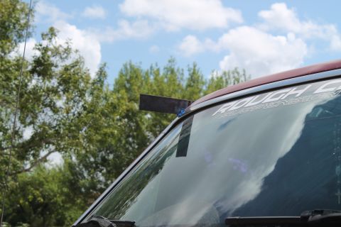 1990 Ford Bronco - A custom metal light mount is attached to the windshield frame with tape, obscuring part of the 'ROUGH COUNTRY' decal.