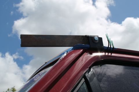 1990 Ford Bronco - Custom bracket and wiring attached to the roof of a red vehicle against a cloudy sky.