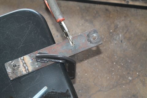 1990 Ford Bronco - A metal bracket is being welded to a black surface, with a clamp holding it in place.