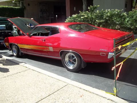 1970 Ford Ranchero - This red 1970 Ford Torino GT features a distinctive gold stripe along its side and a partially open hood.