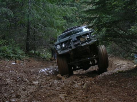 1991 Ford Bronco - An off-road vehicle tackles a challenging muddy path through a dense forest.