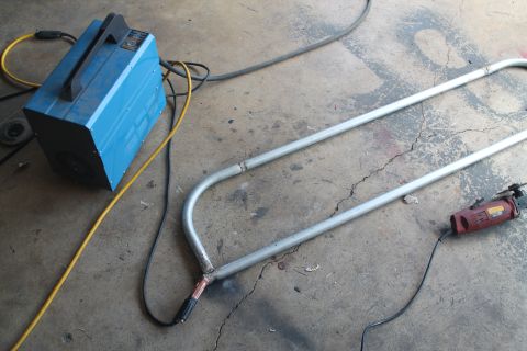 1990 Ford Bronco - Welding equipment and metal tubing are laid out on a concrete floor, suggesting fabrication work.