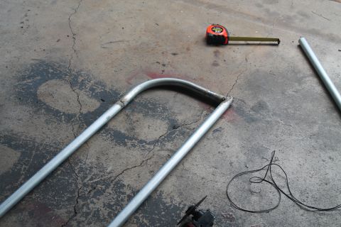 1990 Ford Bronco - Metal tubing and a tape measure are on a concrete surface, suggesting fabrication or repair work.