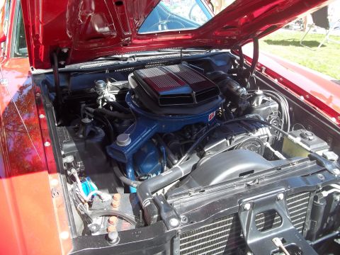 1970 Ford Ranchero - The engine bay of a red 1970 Ford Ranchero is shown with the hood open, revealing the V8 engine and surrounding components.