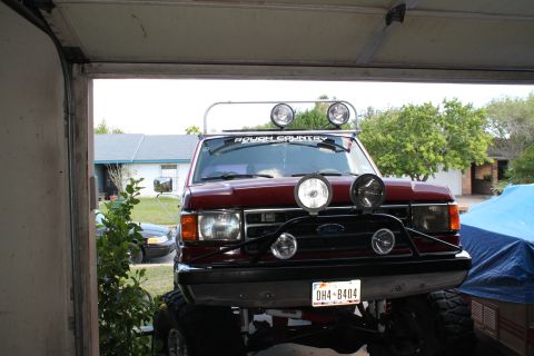 1990 Ford Bronco - This lifted Ford F-Series truck is parked in a garage, equipped with multiple auxiliary lights and a roof rack.