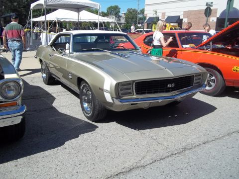 1970 Ford Ranchero - A gold 1969 Chevrolet Camaro SS is parked next to other vehicles under a tent.