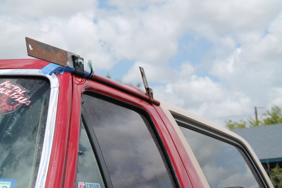Custom metal bracket attached to roof of red SUV, blue tape visible