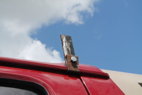 1990 Ford Bronco - A close-up view of a custom-mounted metal bracket on the roofline of a red vehicle against a blue sky.