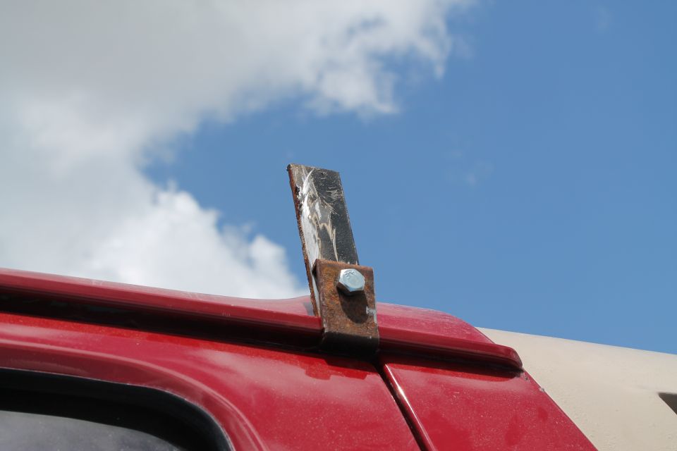 Custom metal light mount bolted to red vehicle roof edge