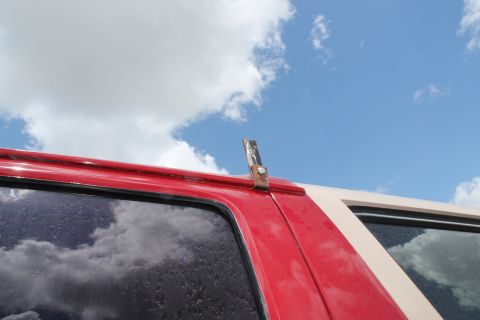 1990 Ford Bronco - A metal bracket is attached to the rain gutter of a red and tan vehicle under a cloudy sky.