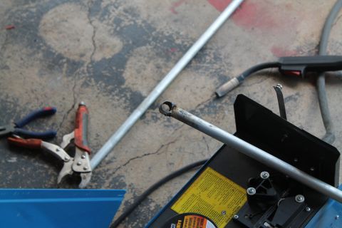 1990 Ford Bronco - A metal pipe is being cut with a grinder, with tools and welding equipment visible in the background.